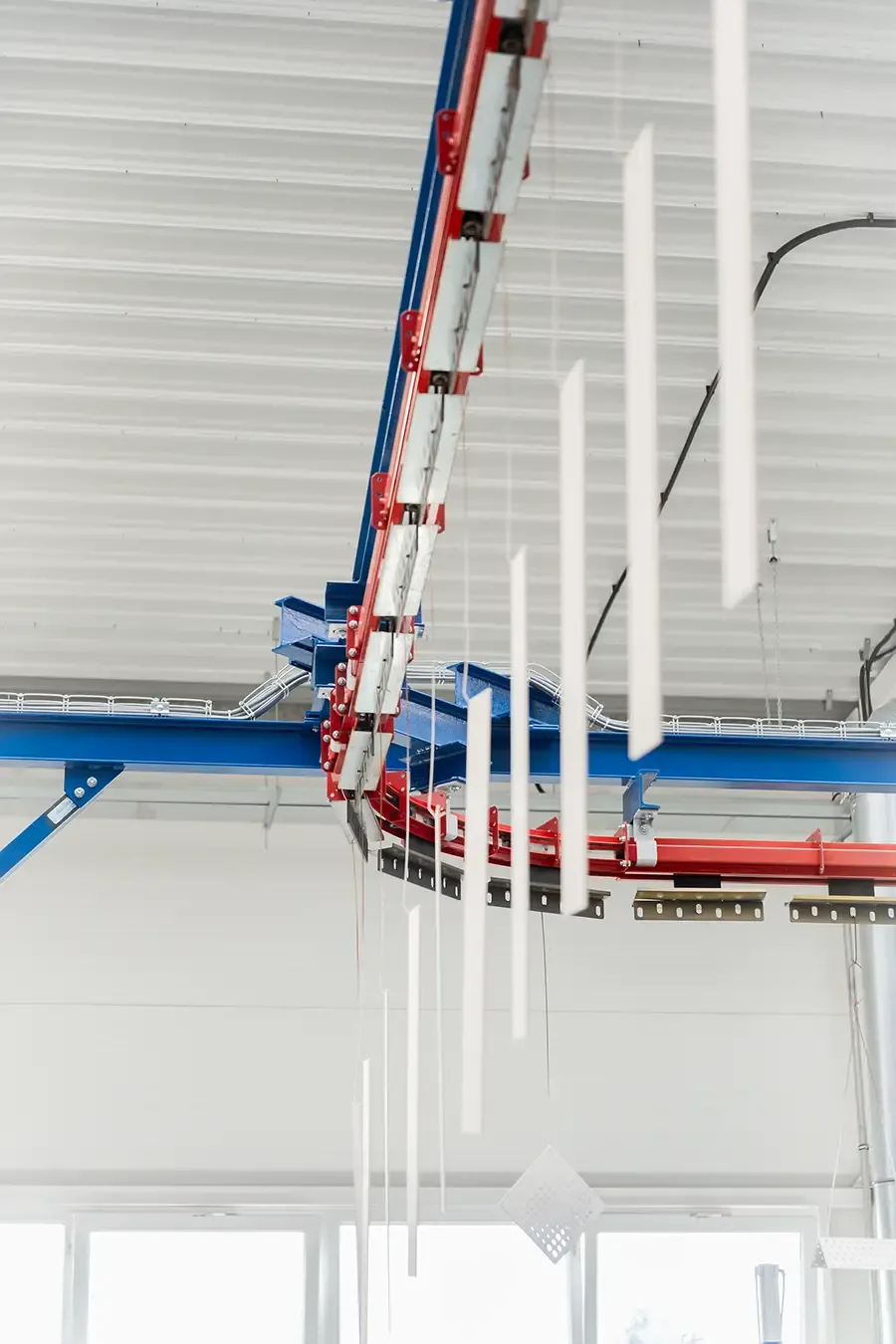 Bílé kovové díly visící na podvěsném dopravníku